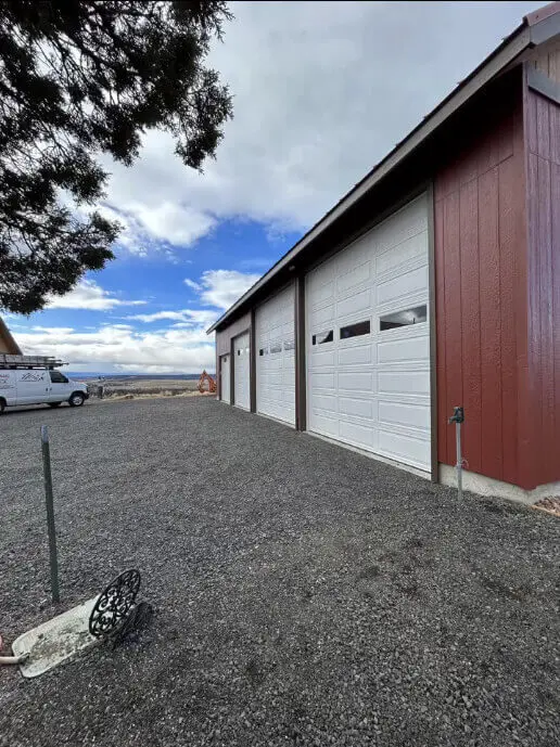 Professionally painted white garage doors on a red barn-style shop in Central Oregon.