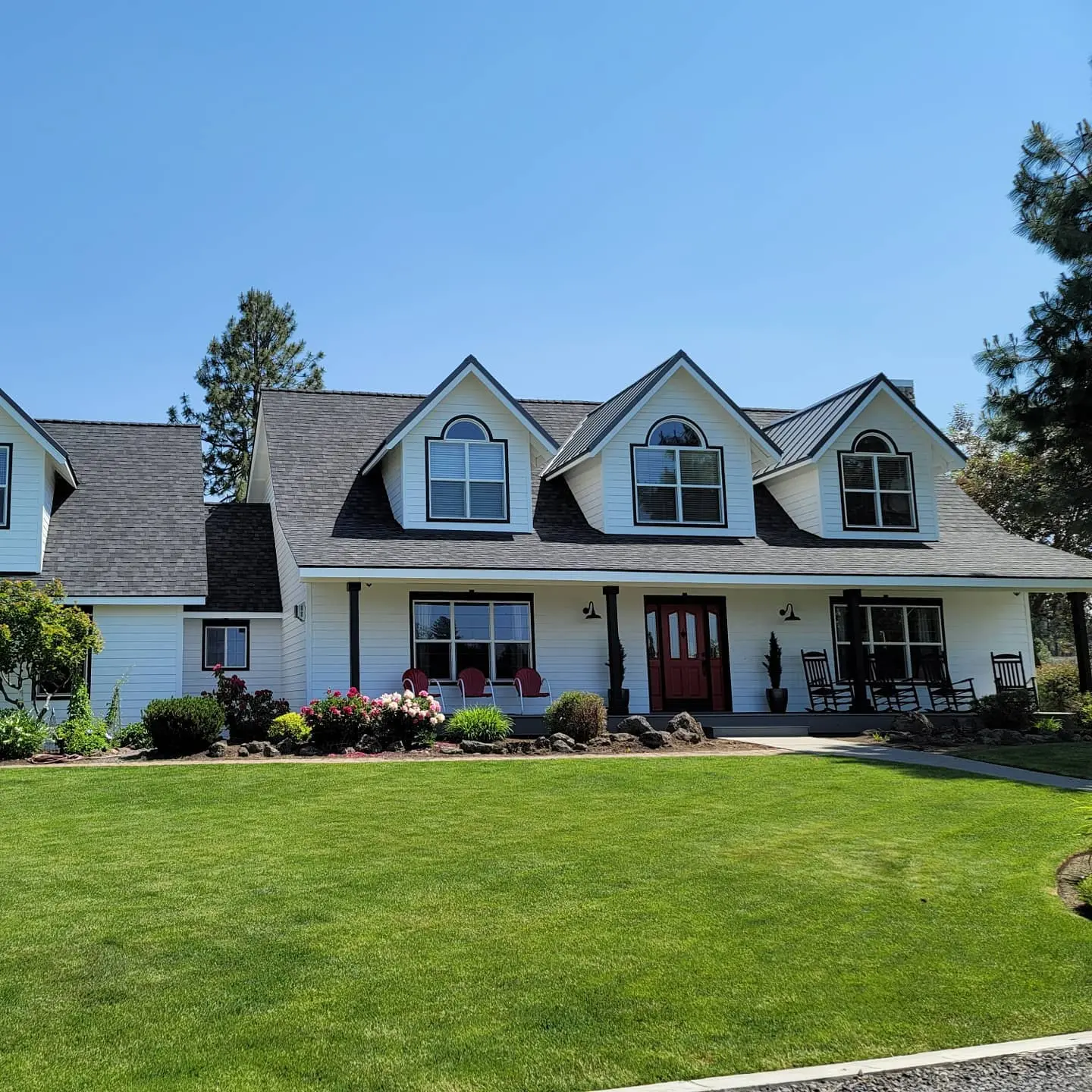 Full front view of a refreshed residential home in Bend with white siding, black pillars, and a red door.